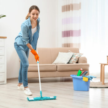 Young woman washing floor with mop in living room. Cleaning service