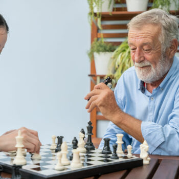 Elderly playing chess with nurse caregiver in nursing home for leisure